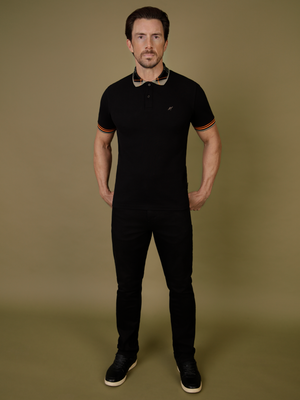 A man wearing the black bali polo, with mishmash black denim jeans.