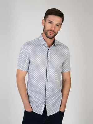 A man wearing a short sleeve white and sky shirt with a geometric print. Menswear UK.