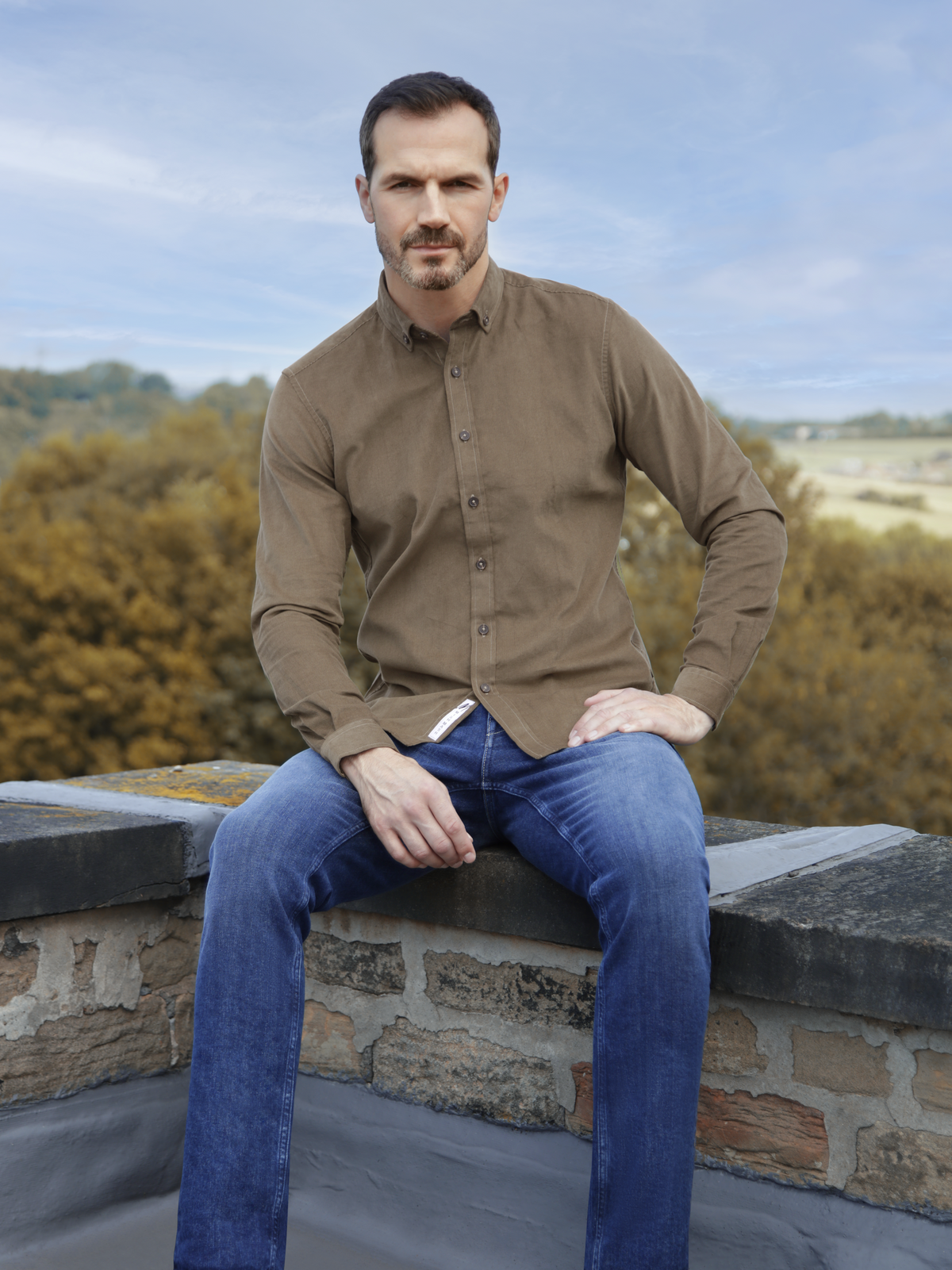 a man wearing a long sleeved cord khaki shirt with mishmash denim jeans.
