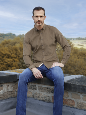 a man wearing a long sleeved cord khaki shirt with mishmash denim jeans.