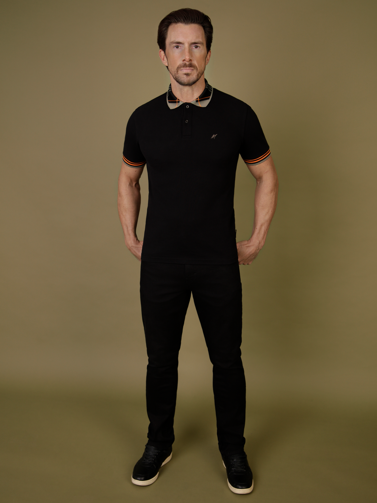 A man wearing the black bali polo, with mishmash black denim jeans.