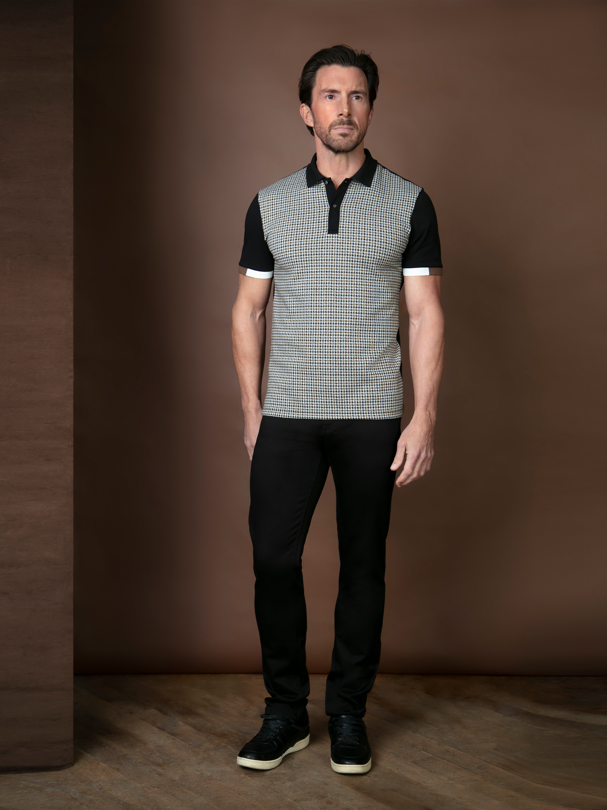 Man wearing a jacquard hounds tooth polo, with black jeans.