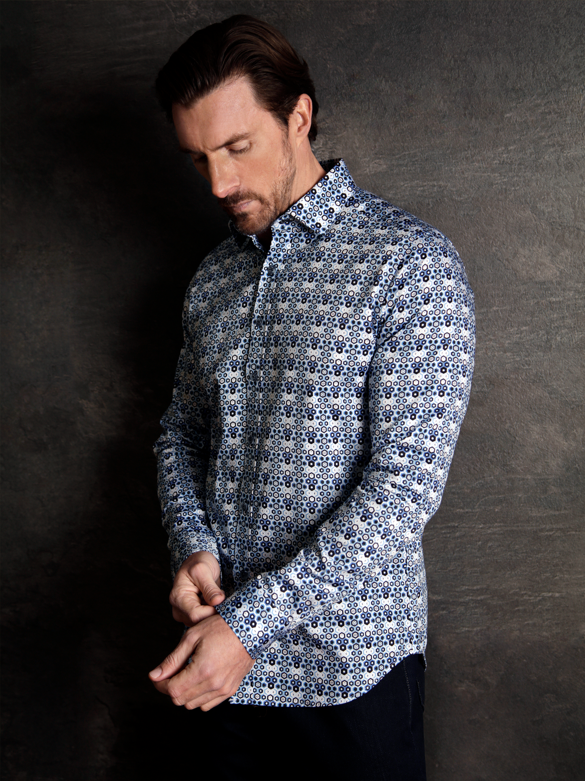 Man wearing a luxurious long sleeve platinum navy and blue shirt with a geo-metric pattern on a textured background.