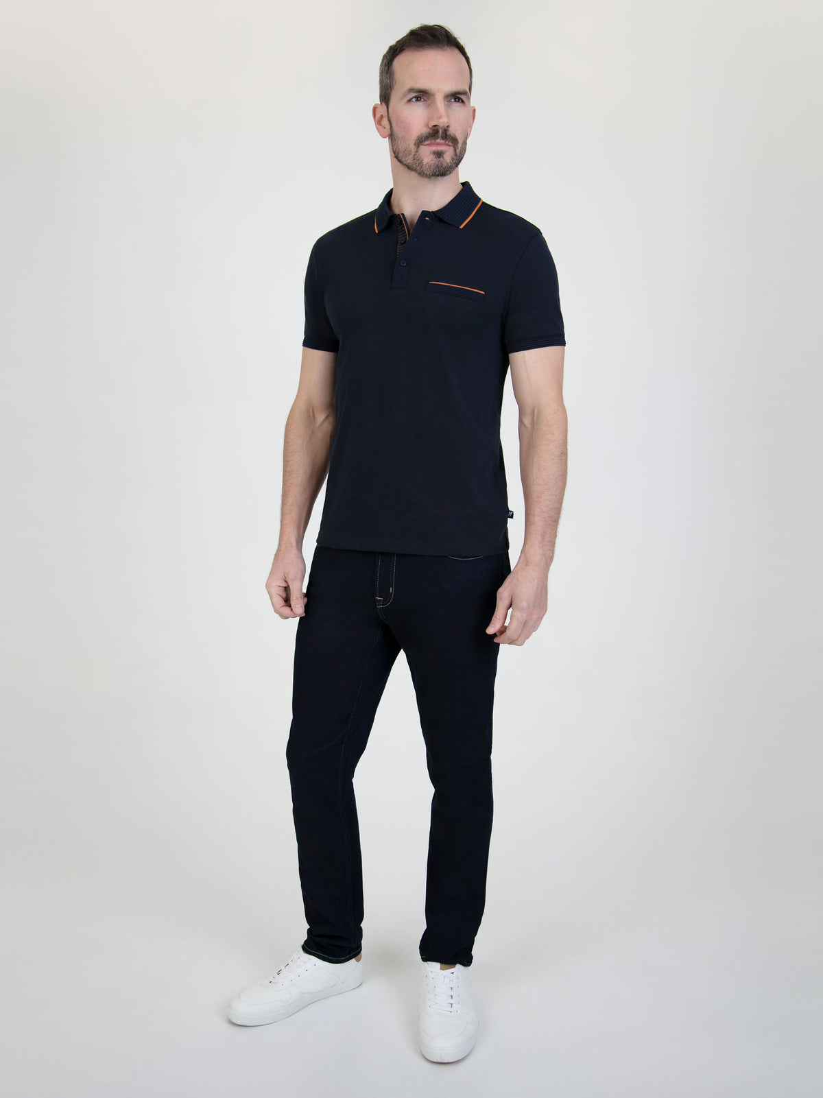 Man wearing a Tonto Navy short-sleeve polo shirt with stylish details, paired with dark jeans and white sneakers.
